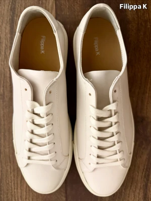 Beige sneakers från Filippa K - Stilrena vita sneakers i mjukt skinn med en ren och tidlös design. En modell som lyfter varje outfit – diskret, elegant och alltid rätt.  Skick: Nya Storlek: 44 Färg: Vit Nypris: ca 2 500–3 000 kr The Label Drop-pris: 1 700 kr  The Label Drop – Premium kvalitet för alla.