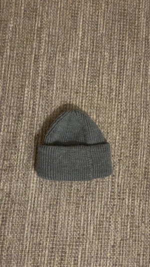 Grå stickad mössa - En enkel och stilren grå mössa med ribbad struktur. Stickad modell med uppvikt kant som ger en klassisk look. Perfekt för kyliga dagar och passar till de flesta outfits.