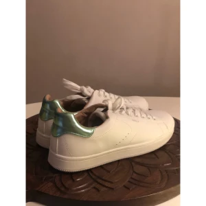 Vita sneakers från ONLY med metallicgrön detalj, 38. - Snygga vita sneakers från ONLY med klassisk rund tå och snörning. Skorna har en unik metallicgrön detalj på hälen som ger en cool touch. Tillverkade i syntetmaterial med platt sula, perfekta för dig som vill sticka ut lite extra. Storlek 38