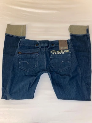 Mörkblå G-Star jeans - Lågmidjade G-Star jeans, strl 28 längd 34 (skulle säga S, se mått). Mått: midjemått tvärs över 40 cm, Innerbenslängd 80 cm när de är vikta som på bilden.