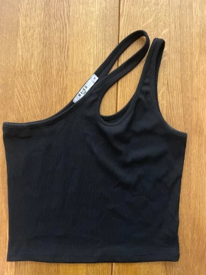 Topp med en axel, croppad - Svart från NAKD