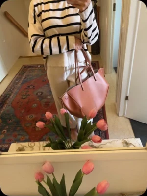 Brun handväska i skinn - Snygg handväska i ljusbrun skinn med stilren, geometrisk form och två handtag. Väskan är rymlig och har minimalistisk design utan synliga detaljer eller mönster. Perfekt för dig som gillar en clean och modern look. Färgen är i textured camel vilket ser ut som kastanjebrun. 