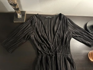 Svart omlotttopp från Stradivarius - Säljer en svart omlotttopp från Stradivarius i storlek XS. Klänningen har plisserat tyg, trekvartsärm och knytband i midjan för en snygg passform. Perfekt för dig som gillar stilrena och trendiga plagg med cool struktur.