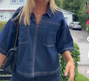 Mörkblå denimskjorta  - Snygg mörkblå denimskjorta från Kappahl i storlek XS. Skjortan har korta ärmar, två stora bröstfickor och kontrastsömmar som ger en cool look. Modellen är loose fit med v-ringad hals och klassisk krage. Perfekt att styla med jeans eller kjol.