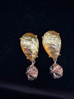 Unika droppformade örhängen i guld - Säljer ett par coola droppformade örhängen i guldtonad metall med en glittrig, texturerad yta. De har en hängande detalj med rutigt mönster som ger extra edge. Perfekta för dig som gillar statement-smycken och vill sticka ut.