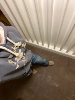 Abercrombie & Fitch Hoodie - Snygg grå hoodie från Abercrombie & Fitch med broderad logga och text i beige på bröstet. Tröjan har en stor huva med beige insida, grova snören och en klassisk magficka. Tillverkad i mjuk bomull. Sitter som en M. Inga defekter alls på tröjan. Om du undrar något är det bara att skriva🙌