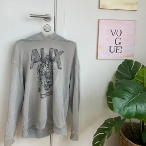Grå hoodie med leopardtryck från Alix - Säljer en grå hoodie från Alix med stort leopardtryck och texten 'ALIX THE LABEL' framtill. Tröjan har huva, långa ärmar och ribbade muddar. Perfekt för dig som gillar coola djurmotiv och streetstyle. Storlek M plus har lite håll vid armarna men tror dom va så när jag köpte 🌸