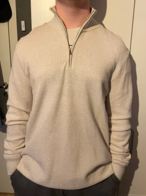 Beige stickad half zip-tröja  - Snygg beige stickad tröja från Kappahl i storlek L. Tröjan har en half zip-dragkedja vid kragen och är långärmad med ribbade muddar. Bara använd en gång och köpt för 499kr