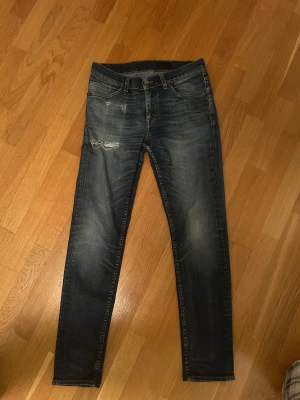 Tiger of Sweden jeans, Style Evolve. - Snygga mörkblå jeans från tiger of Sweden med slimfit passform och slitningar på vänster lår. Klassisk femficksmodell, med bruna sömmar och läderpatch bak i midjan. Jeansen har en tvättad look och är tillverkade i jeansmaterial med dragkedja och knapp. Kontakta vid eventuella frågor!😁