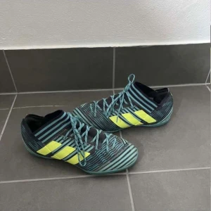 Adidas Nemeziz randiga inomhus fotbollsskor - Säljer ett par Adidas Nemeziz inomhus fotbollsskor med coolt randigt mönster i turkos, svart och neon-gult. Skorna har snörning och låg profil, perfekt för dig som vill sticka ut på planen. Tillverkade i syntetmaterial för bra grepp och komfort.