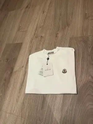 Vit t-shirt från Moncler i mjuk bomull med klassisk rund hals och korta ärmar. På bröstet sitter Monclers ikoniska broderade logotyp i vitt, rött och blått. Stilren och enkel design som passar till allt.