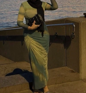 Grön långklänning med rynkdetalj - Snygg långklänning i olika gröna nyanser med rynkdetalj längs ena sidan. Klänningen har långa ärmar och en tight passform som framhäver siluetten. Perfekt för dig som vill sticka ut med en unik look.