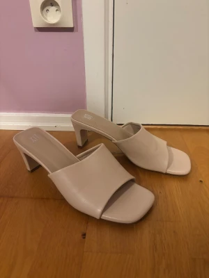 Beige klackade sandaler från XIT - Stilrena beige sandaler från XIT med öppen tå och fyrkantig framdel. Skorna har en bred rem över foten och en snygg låg klack som ger en modern look. Tillverkade i syntetmaterial och perfekta för att lyfta vilken outfit som helst.