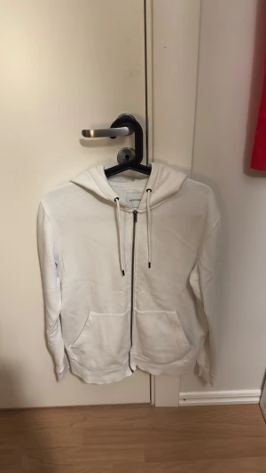 Zip-hoodie   - Vit hoodie från Jack & Jones i storlek S. Mjuk insida, dragkedja framtill, två fickor och justerbar huva med snören. Klassisk och enkel design, perfekt för chill dagar. Materialet är bomullsmix som känns skönt mot huden.
