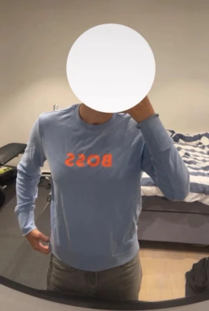 Ljusblå BOSS sweatshirt XS - Snygg ljusblå sweatshirt från BOSS i bomull med orange BOSS-tryck på bröstet. Tröjan har rund hals, långa ärmar och en relaxed passform. Perfekt för chill dagar och enkel att matcha med jeans eller joggers. Det är någon fläck, kan gå bort i tvätt men ej säker. Inköp på room 1003 jätte fin