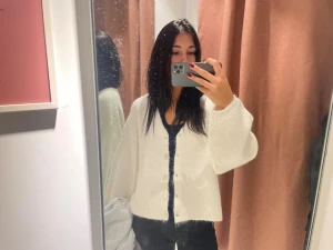 Vit stickad kofta med knappar Gina  - Supermysig vit stickad kofta med pärlemorknappar och ballongärmar. Koftan har en croppad passform och är perfekt att slänga över en topp. Mjuk och fluffig känsla, passar till allt och ger en chill vibe.