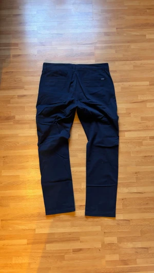 Mörkblå raka kostymbyxor - Snygga mörkblå kostymbyxor med rak passform och klassiska fickor bak. Byxorna har en stilren look och är tillverkade i ett mjukt material som ger en skön känsla. Perfekt för dig som gillar en clean och enkel stil.