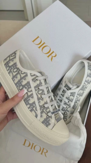 Dior Oblique sneakers i grått och vitt - Snygga Dior Oblique sneakers med grått och vitt monogrammönster, vita snören och platt sula. Skorna har tydlig Christian Dior-logga på plösen och sidan. Tillverkade i canvas med detaljer i skinn och gummisula. Perfekta för dig som gillar lyxig streetstyle.