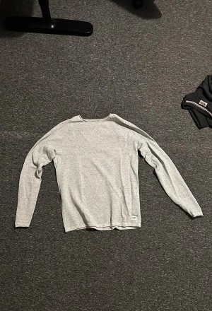Grå långärmad tröja Jack & Jones - Snygg grå långärmad tröja från Jack & Jones i storlek M. Tröjan är unik då halsen är rundad och materialet är unikt. Det passar perfekt som en unik bit i outfiten men ändå clean💯🙌 Finns även beige om ni är intresserade😉