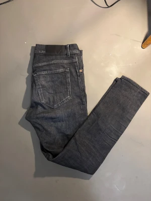 Tiger of Sweden svarta jeans Evolve 31/32 - Snygga svarta jeans från Tiger of Sweden, modell Evolve. De har klassisk femficksdesign, smal passform och raka ben. Jeansen är tillverkade i Italien och har subtila slitningar för en cool look. Perfekta för dig som gillar stilrena och moderna jeans.