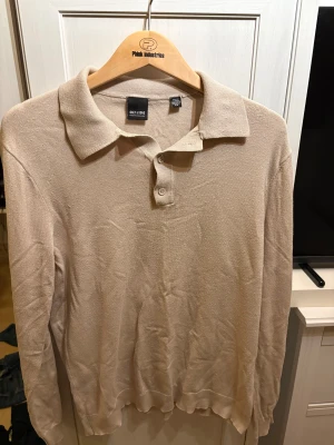 Beige pikétröja grisch från Only & Sons - Snygg beige pikétröja från Only & Sons med klassisk krage och 3 knappar framtill. Tröjan är långärmad och har en mjuk, stickad känsla som gör den skön att bära. Perfekt för dig som gillar stilrena och enkla plagg med en chill vibe.