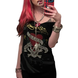 Ed Hardy svart t-shirt med tryck - Svart t-shirt från Ed Hardy med ikoniskt dödskalle- och hjärttryck framtill, glittriga detaljer och guldfärgad logga. Kortärmad modell med snörning och öppen rygg för extra edge. Perfekt för dig som gillar statement-plagg och streetstyle. Tappat en del kristaller men syns knappt vid användning😍