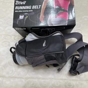 Crivit löparbälte med flaska - Säljer ett svart och grått löparbälte från Crivit med justerbart spänne och en 650 ml vattenflaska. Bältet har praktiska fickor för småsaker och är perfekt för löprundan eller promenaden. Snygg och sportig design med reflexdetaljer.