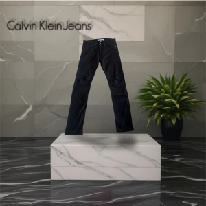 Svarta skinny jeans Calvin Klein - Svarta skinny jeans från Calvin Klein Jeans med slitna detaljer vid knäna. Klassisk femficksmodell med silverfärgade nitar och logotyp på bakfickan samt patch i vitt vid linningen. Midja tvärsöver 42cm, innerbenslängd 81cm