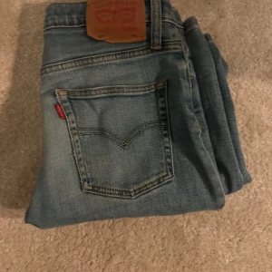 Levi's 501 ljusblå jeans straight fit - Asfeta Levis 501 i barnstorlek 14-16, sitter ungefär som en 28 i midjan och 30-31 i längd. Köpta för 1.5 år sedan och andvönda vilket skapat snygga slitningar (de större är från fabrik). Skriv för frågor eller bilder!🍾
