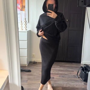 Svart ribbad långkjol - Säljer en svart ribbad långkjol med tight passform. Kjolen är stickad och har en mjuk, elastisk midja som sitter skönt. Den är enkel och stilren, perfekt för dig som gillar minimalistisk look och vill ha något som är både bekvämt och snyggt.