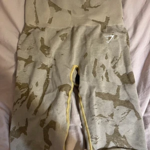Grå camo leggings från Gymshark - Snygga grå leggings från Gymshark med camouflagemönster och hög midja. De har gul kontrastsöm längs insidan av benen och är tillverkade i ett stretchigt material som passar perfekt för träning. Diskret Gymshark-logga på höften. Sömmen gått av bak