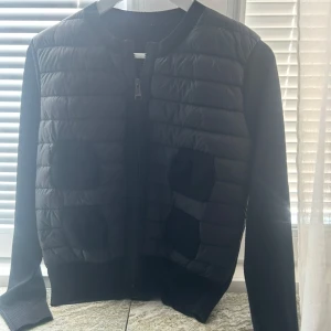 Svart quiltad cardigan jacka - Svart cardigan jacka med quiltad framsida och två stora fickor. Jackan har dragkedja framtill och är långärmad med ribbade muddar. Perfekt för lager-på-lager och en clean look.