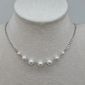 Silverhalsband med pärlor - Stilrent halsband med silverfärgad kedja och sju vita pärlor i olika storlekar framtill. Kedjan har klassisk länkdesign och pärlorna ger en elegant touch. Perfekt accessoar för att lyfta din outfit med en tidlös känsla.