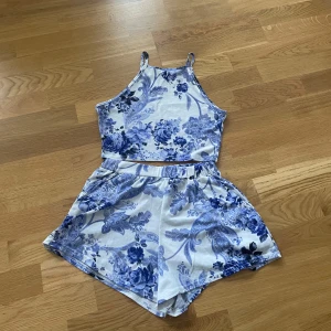 Blommig blå och vit set - Säljer en söt set med smala axelband och blommigt blått och vitt mönster. Toppen är croppad och har en avslappnad passform, perfekt för varma dagar. Materialet känns mjukt och lätt mot huden.