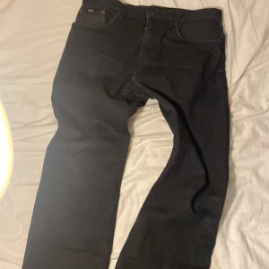 Svarta stretchjeans från Hugo Boss - Svarta jeans från Hugo Boss med stretch för extra komfort. Klassisk femficksmodell med diskret Boss-logga på fickan och bak vid linningen. Snygg, stilren look som passar till det mesta. Jeansen har raka ben och normal passform.