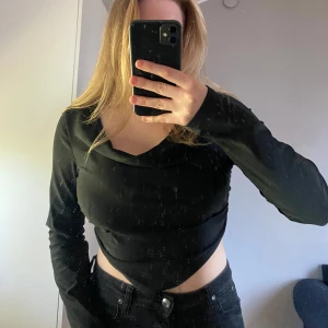 Svart långärmad croppad topp - Säljer en svart långärmad topp med croppad passform och spetsig nederkant. Toppen har en snygg v-ringad halsringning som kan stylas på olika sätt. Perfekt att matcha med höga jeans för en trendig look.
