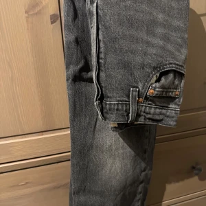 Levi's 501 svarta jeans Ribcage straight - Svarta Levi's 501 jeans med klassisk femficksdesign, knäppning med knappar och hög midja. Jeansen är raka i modellen och är uppsydda i butik. Innerbenslängd 68,5 cm. Helt nya och tvättats en gång men aldrig använda.