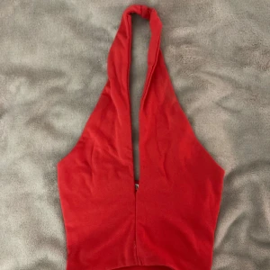 Röd halterneck topp från Zara - Säljer en röd halterneck topp från Zara i mjuk bomull. Toppen har djup v-ringning framtill och kan stylas med korsad nacke. Perfekt för dig som gillar trendiga och enkla plagg med snygg passform.
