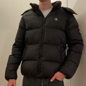 Pufferjacka från Calvin Klein - Säljer min pufferjacka från Calvin Klein! Köpt i slutet av förra vintern och endast använd i några veckor innan det blev för varmt. Jackan är stilren, varm och väldigt bekväm. Den är i princip i nyskick utan några tecken på slitage. Luvan är avtagbar, så du kan välja om du vill ha den på eller inte. Nypris: 2 799 kr (Säljer den då jag hellre vill ha en kavaj)