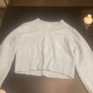 Ljusblå croppad stickad tröja - Superfin ljusblå stickad tröja med v-ringning och bred ribbad kant nertill. Modellen är croppad och har långa ärmar, perfekt för lager på lager. Mjuk och skön känsla, passar till både jeans och kjol. Den är använd men inga skador!