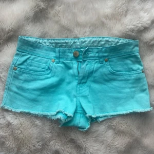 Turkosa jeansshorts med rå kant - Snygga turkosa jeansshorts med fransig rå kant och klassisk femficksdesign. Shortsen har knapp och dragkedja framtill samt hällor för bälte. Perfekta för varma dagar och har en normal passform med låg midja.