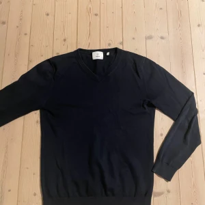 Tröja svart  - Pris kan diskuteras En stilren svart v-ringad tröja från Bläck. Tröjan har lång ärm, ribbade muddar och är tillverkad i mjuk bomull. Perfekt för dig som gillar en clean och klassisk look.