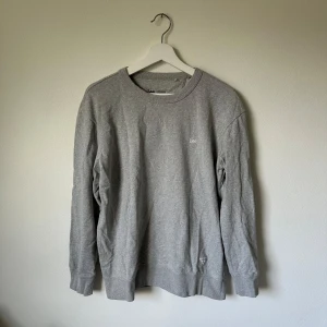 Grå sweatshirt från Lee i bomull - Klassisk grå sweatshirt från Lee i 100% bomull med regular fit. Tröjan har rund halsringning, ribbade muddar och diskret Lee-logga på bröstet. Perfekt basic att ha i garderoben för en avslappnad stil. 2J7