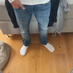 Blå Jack&jones jeans  - Snygga blå jeans från jack&jones i storlek 32/34. Jeansen har en slim passform och klassisk femficksdesign. De är tillverkade i mjukt denimtyg och har en lätt tvättad look med subtila slitningar. Perfekta för dig som gillar en smalare siluett och stilren känsla.