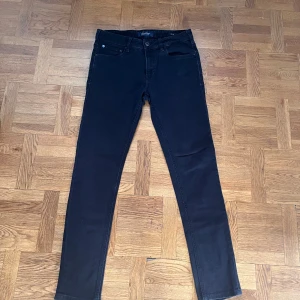 Svarta jeans Scotch & Soda - Svarta slimfit jeans från Scotch & Soda med klassisk femficksdesign och blå korsstygnsdetalj på bakfickan. Jeansen har normal midja och är tillverkade i stretchig bomullsblandning för en tight passform. Perfekta för dig som gillar stilrena och moderna jeans.