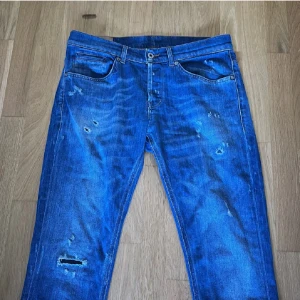 Dondup George jeans  - Säljer ett par blå jeans med slitningar och hål på flera ställen för en cool, avslappnad look. Klassisk femficksmodell med raka ben och normal passform. Jeansen har tydliga slitdetaljer framtill och bakfickor med dekorativ söm.