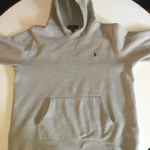 Grå hoodie från Ralph Lauren - Säljer en klassisk grå hoodie från Ralph Lauren med en liten broderad logga på bröstet. Tröjan har en bekväm huva och en känguruficka framtill. Perfekt för en avslappnad stil. Pris kan diskuteras😊