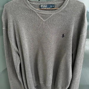 Grå tröja från Polo Ralph Lauren - Säljer en stilren grå tröja från Polo Ralph Lauren i storlek M. Tröjan har rund halsringning, diskret broderad logga på bröstet och är ribbstickad i mjukt material. Perfekt för dig som gillar klassisk och enkel stil.