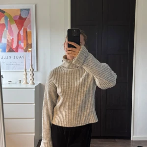 Beige ribbad polotröja - Säljer en beige ribbstickad polotröja med lång ärm och relaxed fit. Tröjan har hög krage och är tillverkad i ett mjukt, stickat material som är perfekt för kyligare dagar. Enkel att styla med både jeans och kjol.