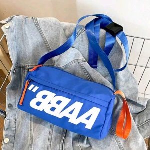 Blå axelväska med vit text - Cool blå axelväska med stor vit text på framsidan och orange detaljer. Väskan har justerbar axelrem och dragkedja i kontrasterande färg. Perfekt för att bära dina viktigaste grejer och ge outfiten en sportig vibe.